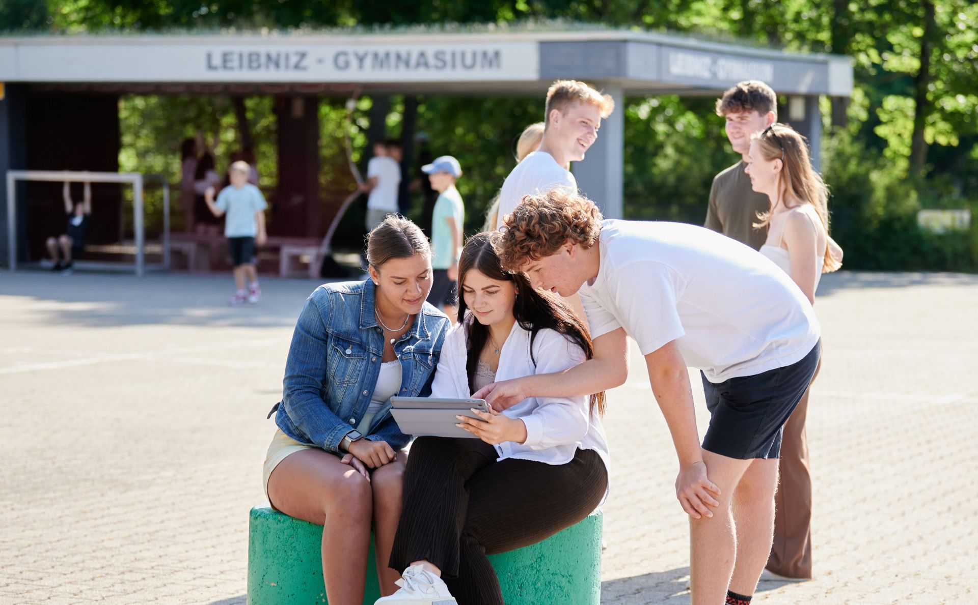 Drei Schüler*innen schauen auf dem Pausenhof gemeinsam in ein Tablet.