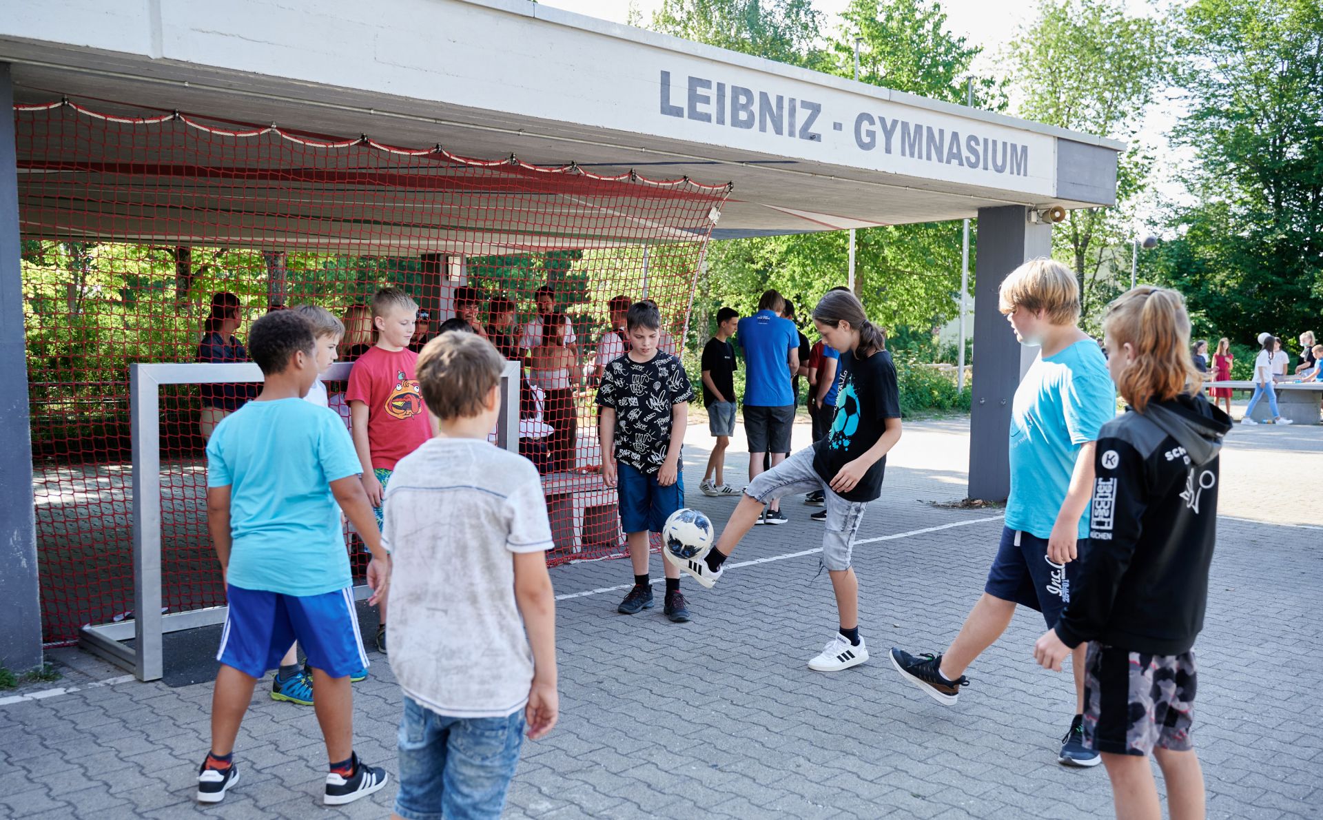 Eine Gruppe Schüler spielt auf dem Pausenhof Fußball im Kreis.